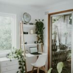 Small desk with a leaning ladder shelf above it for vertical storage - books, a globe and plants in a bright, compact workspace.