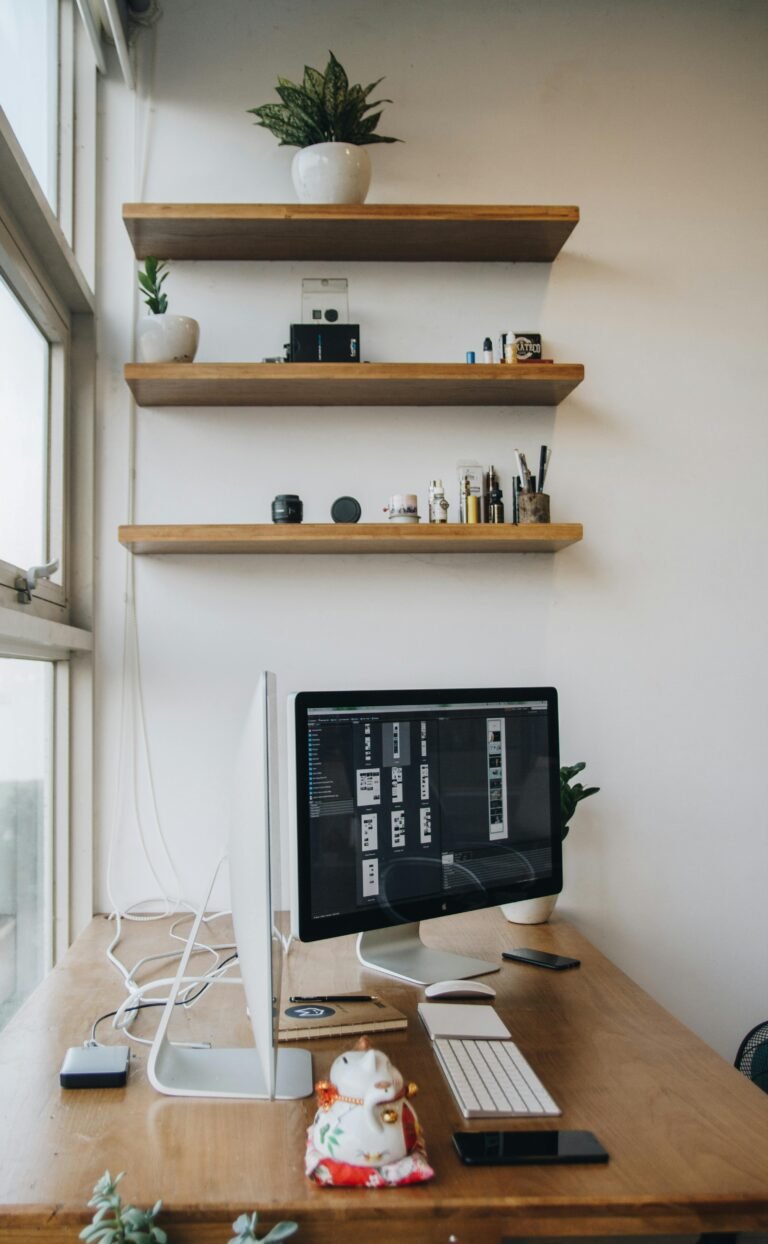 Wooden clamp shelf mounted to the edge of a small desk, holding books and a few accessories above the work surface — adding storage without taking floor space.