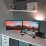 Dual monitor setup on a small white corner desk with two screens side by side