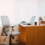 Grey mesh office chair with armrests beside a wooden desk with a laptop