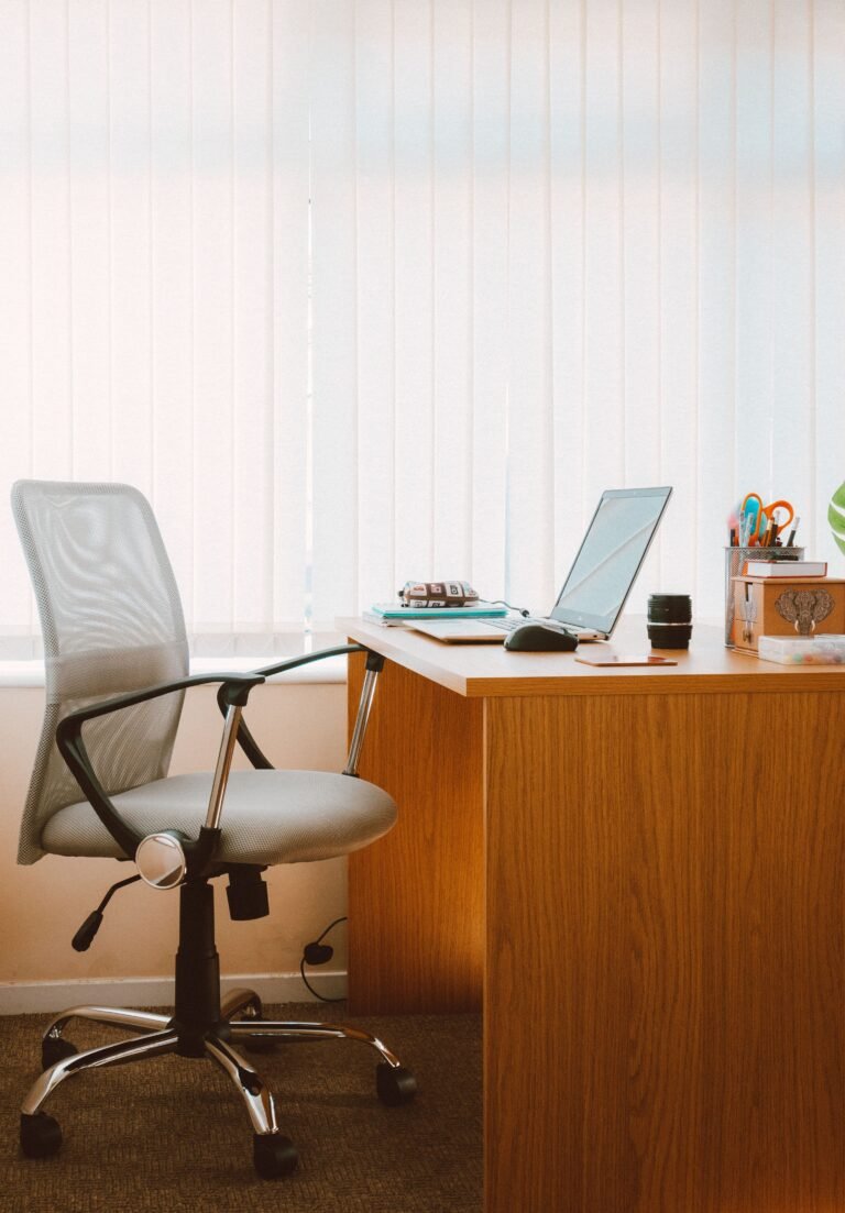Grey mesh office chair with armrests beside a wooden desk with a laptop