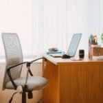 Grey mesh office chair with armrests beside a wooden desk with a laptop